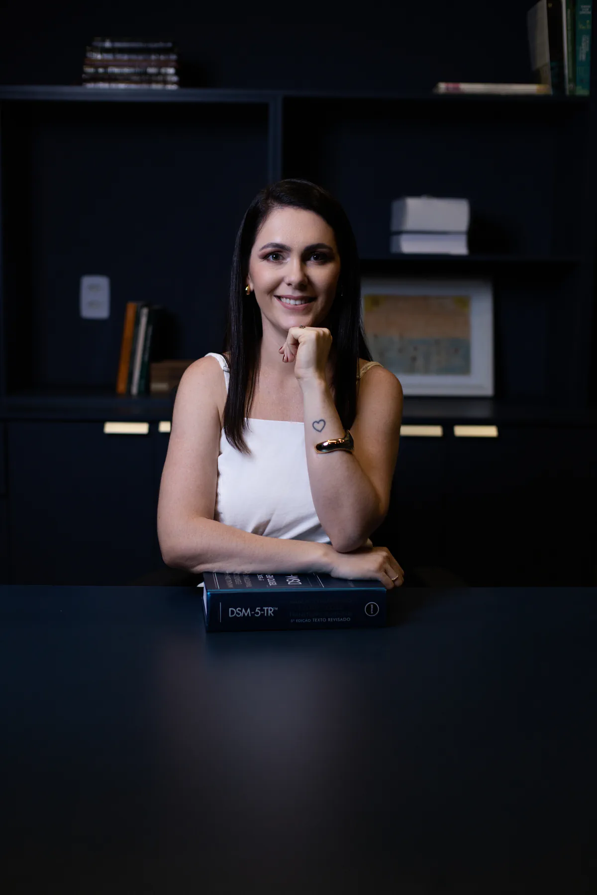 Fabiana Furtili em seu espaço de trabalho, com as mãos apoiadas sobre um livro